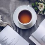 Poetry Readings - White Ceramic Teacup With Saucer Near Two Books Above Gray Floral Textile