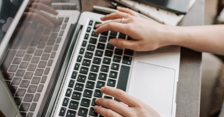 Independent Publishers - From above of unrecognizable woman sitting at table and typing on keyboard of computer during remote work in modern workspace