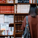 University - Woman Wearing Brown Shirt Carrying Black Leather Bag on Front of Library Books