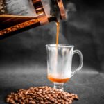 Sunday Roast - Aromatic hot coffee being poured from French press into elegant glass with pile of coffee beans beside on black background