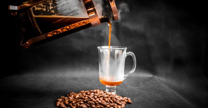 Sunday Roast - Aromatic hot coffee being poured from French press into elegant glass with pile of coffee beans beside on black background