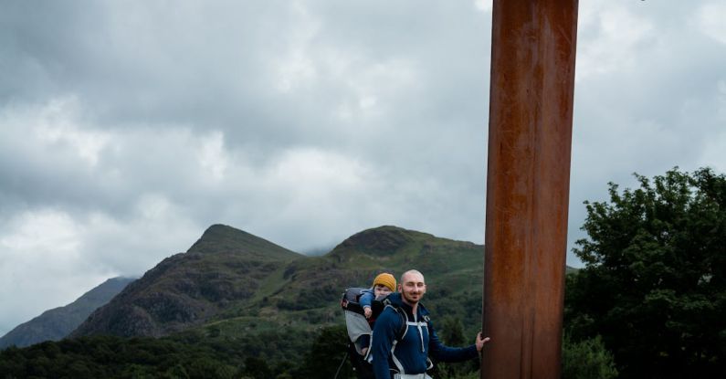 Snowdonia - Man Standing Beside a Giant Sword Near a Body of Water