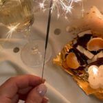 Food Festivals - From above of unrecognizable female with burning Bengal light standing near flowers wineglass and food on tray on white fabric in room with burning candles