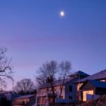 Neighborhoods - A moon rises over a house and a lake