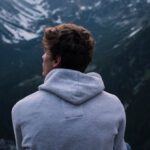 Solo Travelers - A Man in White Hoodie Sitting on a Rock Across the Mountains