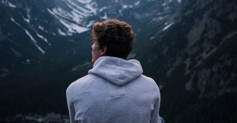 Solo Travelers - A Man in White Hoodie Sitting on a Rock Across the Mountains